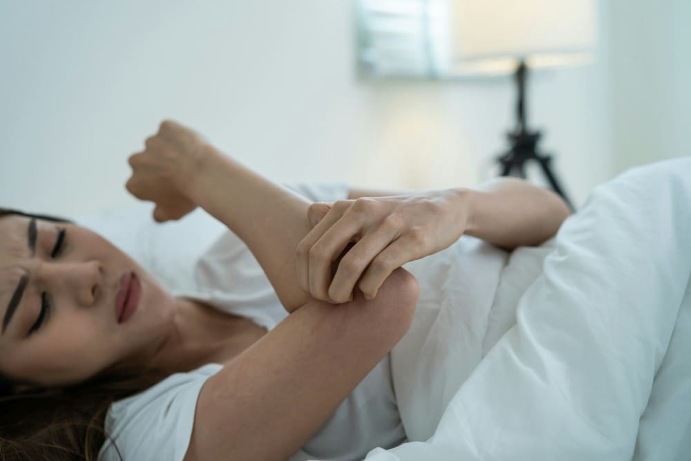 Femme qui se gratte le bras dans son lit
