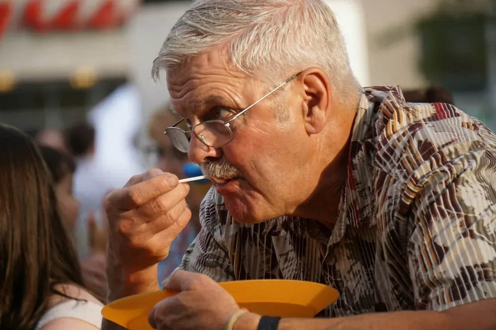 Diabète et cholestérol : un homme portant des lunettes tient une assiette jaune et porte un petit bâtonnet à sa bouche.