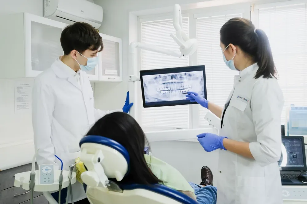 Deux dentistes analysent une radiographie panoramique dentaire avec une patiente assise sur un fauteuil