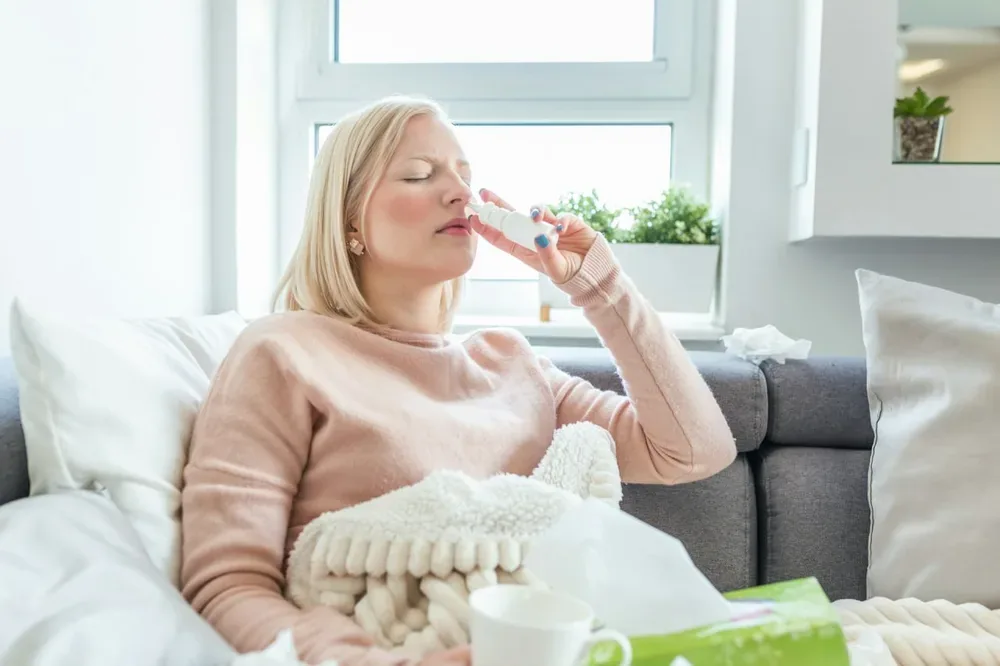Une adulte utilise un spray nasal sur un canapé, dans un contexte de nez bouché.