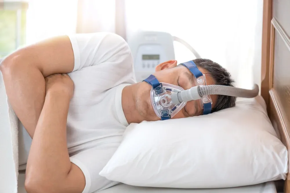 Diabète et apnée du sommeil : un homme dort avec un masque relié à un appareil de pression positive.